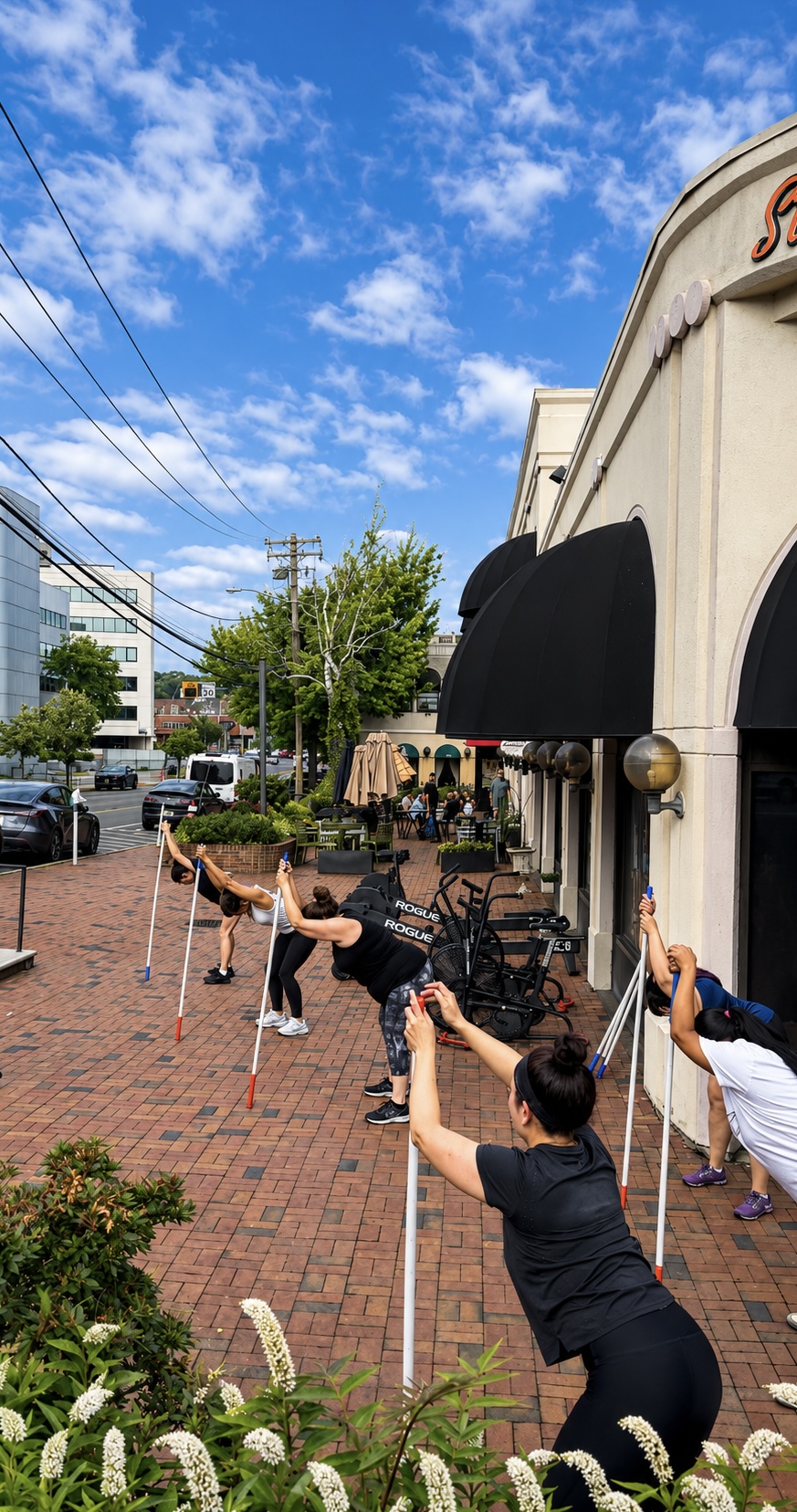 A group of members using PVC poles for an outdoor Stretch & Mobility class in front of the StretchPlusFlex studio in Great Neck Plaza